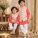 A refined boys' kurta pyjama jacket set crafted in 100% cotton, featuring a vibrant coral pink kurta paired with classic white pyjamas and a beautifully printed ivory Nehru jacket. The jacket is adorned with delicate rose motifs in soft pink with subtle golden botanical detailing, adding an elegant festive touch to the ensemble. The structured jacket brings a polished finish to the traditional kurta pyjama silhouette, while the breathable cotton fabric keeps little ones comfortable throughout the day. Perfect for festive celebrations, weddings, pujas, family gatherings and special occasions.