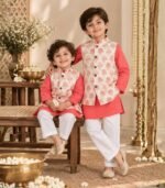 A refined boys' kurta pyjama jacket set crafted in 100% cotton, featuring a vibrant coral pink kurta paired with classic white pyjamas and a beautifully printed ivory Nehru jacket. The jacket is adorned with delicate rose motifs in soft pink with subtle golden botanical detailing, adding an elegant festive touch to the ensemble. The structured jacket brings a polished finish to the traditional kurta pyjama silhouette, while the breathable cotton fabric keeps little ones comfortable throughout the day. Perfect for festive celebrations, weddings, pujas, family gatherings and special occasions.